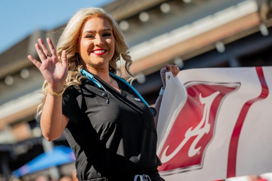 Alabama Nursing student smiles and waves as she walks the homecoming parade. 