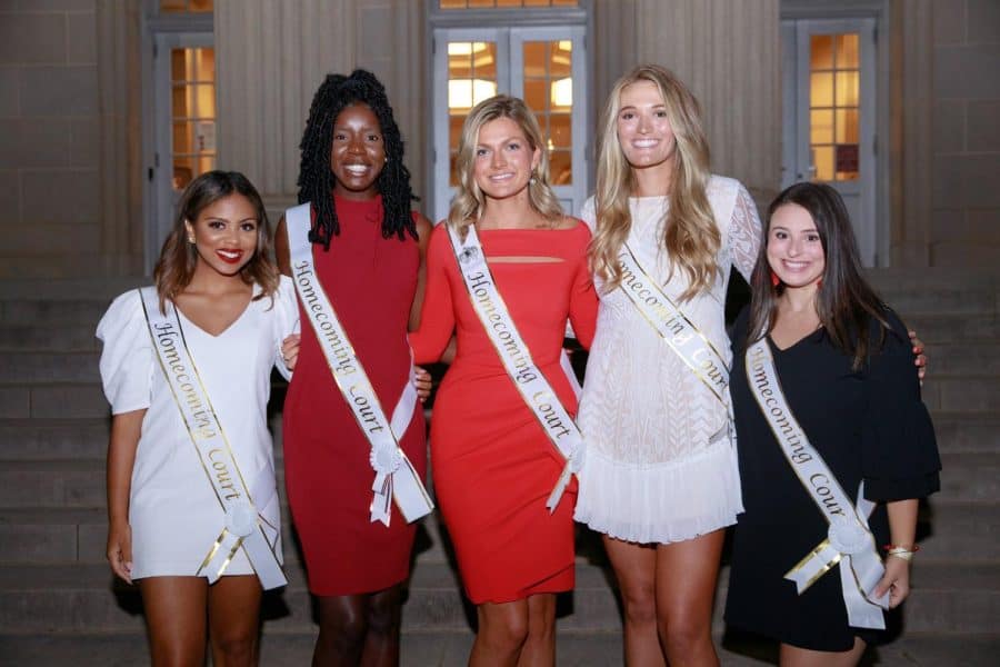 A photo of five women side by side wearing nice dresses and Homecoming Court sashes.