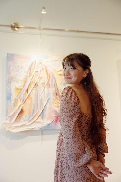 Abi Brewer standing in front of her artwork. Brewer is a speaker at Kentuck Art Center’s event, Spinning Stories: Truths and Tales from Women Creatives.
