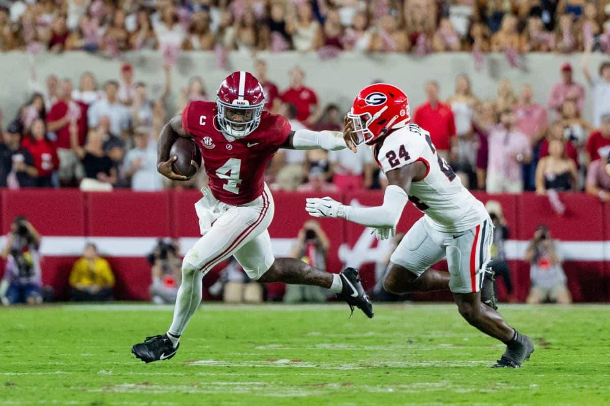 Alabama quarterback Jalen Milroe (#4) stiff arms a Georgia defender.