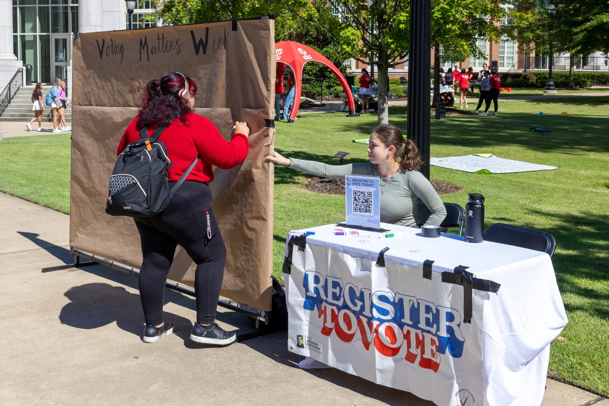 A student signs a "Voting Matters Week" sign after registering to vote.