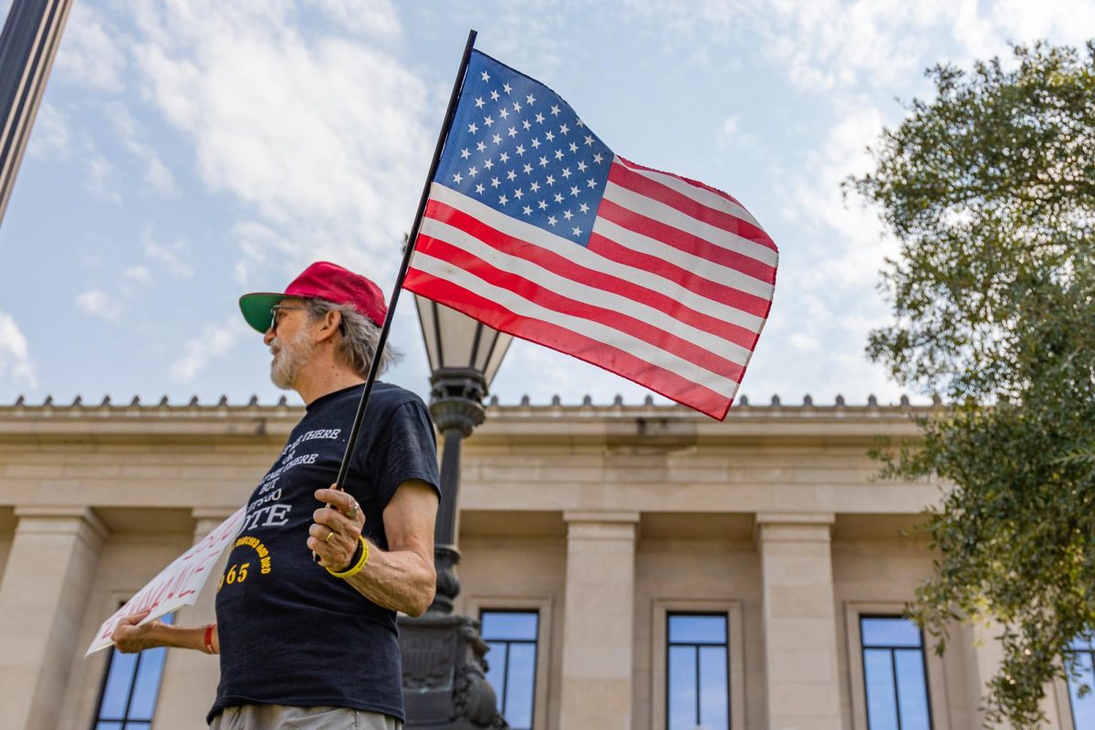 A Tuscaloosa resident carries an American flag and a sign during the protest against troops in D.C. in downtown Tuscaloosa on Sep. 6, 2025.